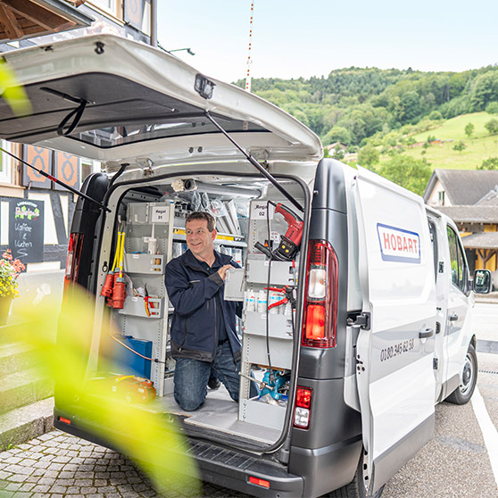 Servisní vozidlo s logem HOBART a otevřenými dveřmi, vybavené nářadím a policemi pro práci v terénu.