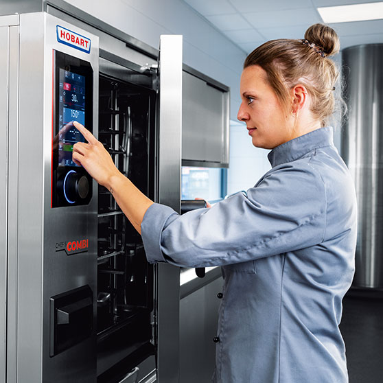 Osoba ovládá dotykový displej zařízení CHEF'S COMBI – s nastavením času a teploty jako „30“ a „150°“, což umožňuje přesné řízení v profesionální kuchyni.