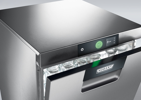 Podstolní myčka HOBART z nerezové oceli s částečně otevřenými dvířky a viditelnými sklenicemi uvnitř, vybavená digitálním ovládacím panelem a zeleným tlačítkem start.