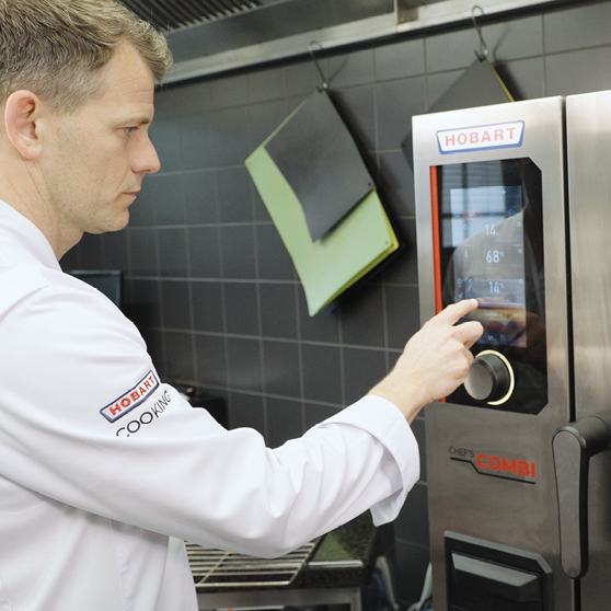 [Translate to cs_CZ:] Chef operating the touchscreen control panel of a HOBART CHEF’S COMBI in a professional kitchen, adjusting settings for precise and efficient cooking workflows.