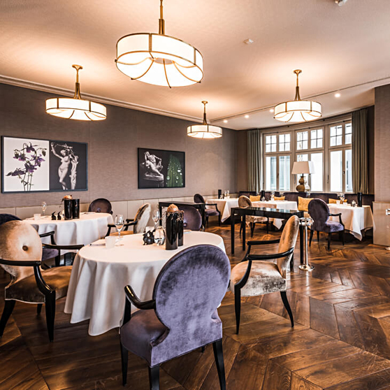Elegantní interiér fine‑dining restaurace s kulatými stoly s bílým prostřením, čalouněnými židlemi a teplým ambientním světlem.