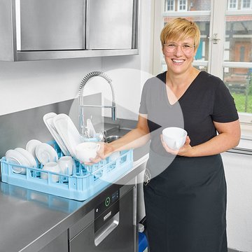 Moderní mycí zóna s nerezovou pracovní plochou a myčkou HOBART, modrý koš s čistým nádobím včetně talířů a misek, pracovník vykládá pro hygienické čištění